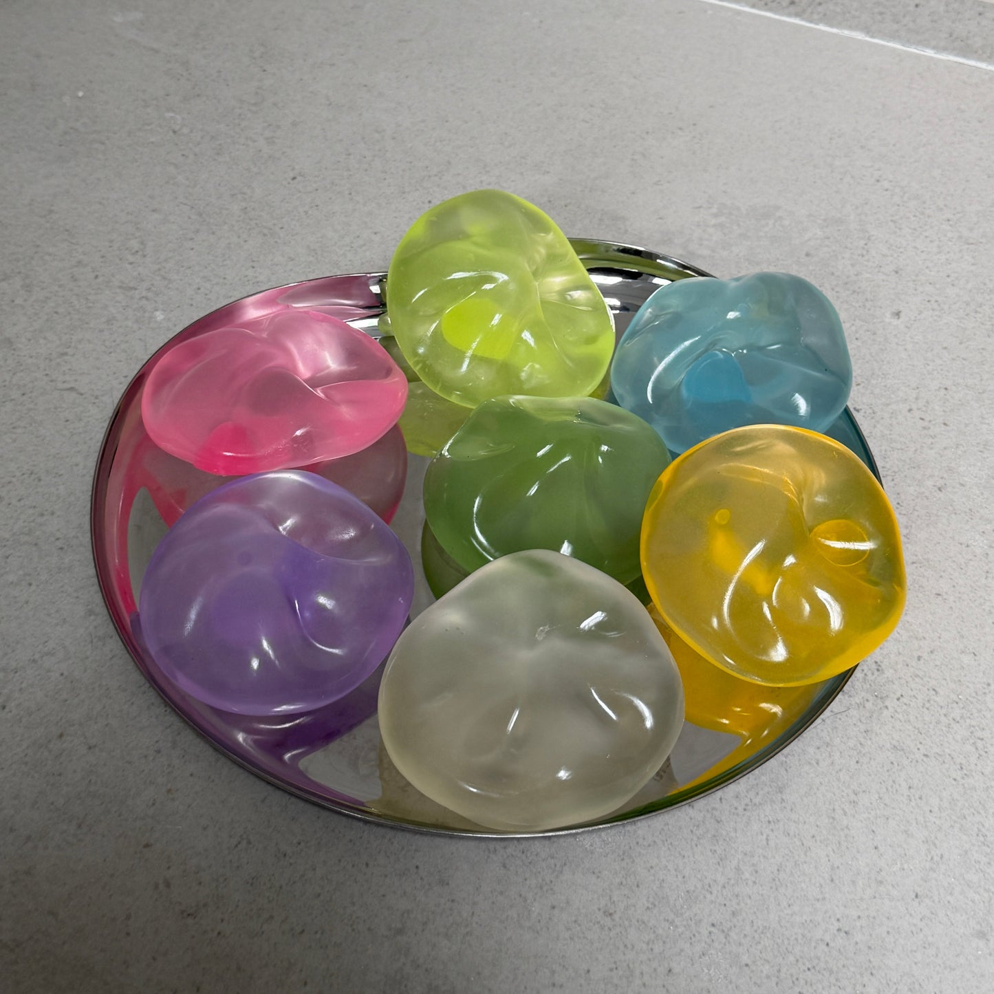 Translucent coconut oil sugar ball squishy stress toys in assorted colors displayed together on a reflective tray.