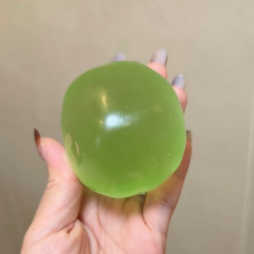 Handheld emerald green coconut oil squishy stress ball with translucent color, medium-firm resistance, smooth glossy surface, and slow rebound.