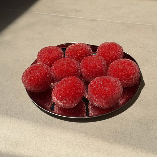 Red shaved ice texture ASMR squishy balls with soft crystal-like surfaces arranged on a metal tray in warm sunlight.