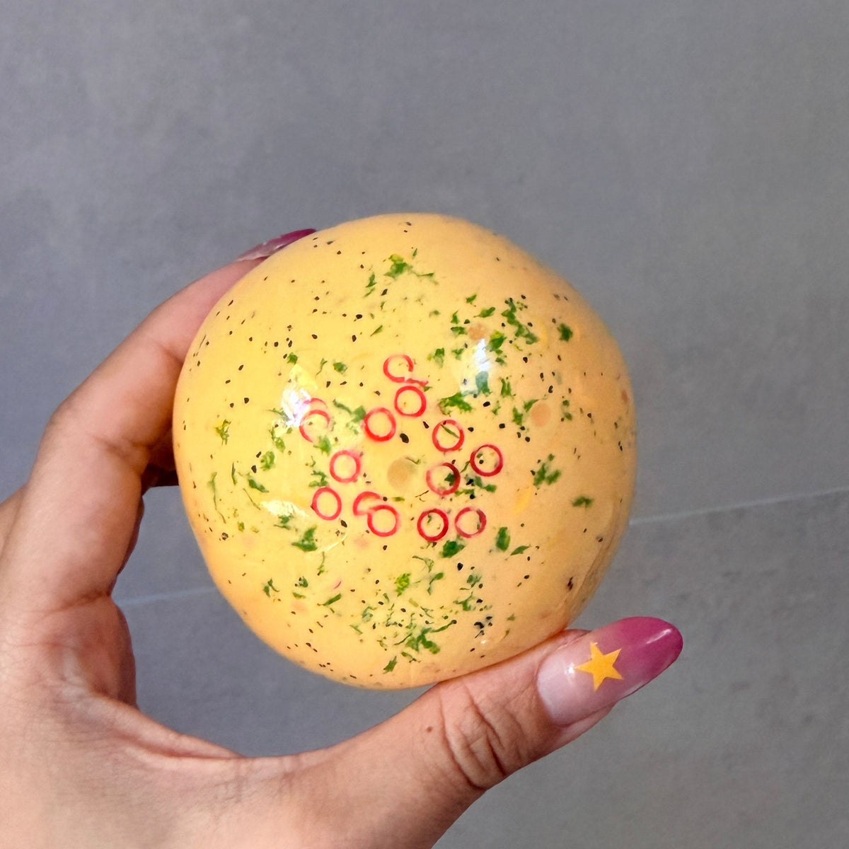 Close-up of a hand holding the Artistic Handmade omelette noisy stress ball with green herb details and red chili rings.
