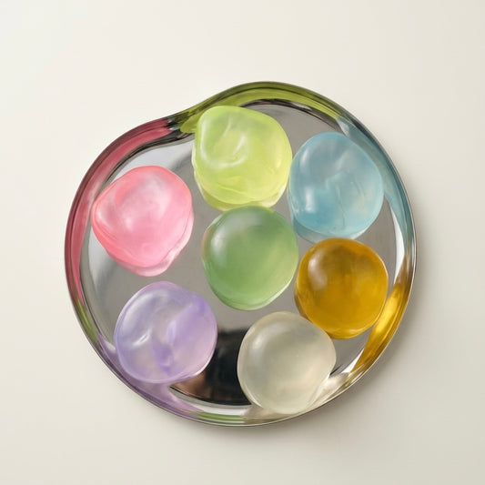 Translucent coconut oil sugar ball squishy stress toys in assorted pastel colors displayed on a reflective tray.