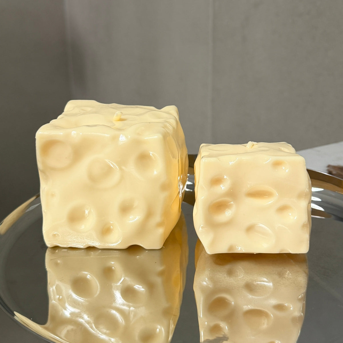 Jumbo and baby cheese squishy stress ball sensory toys displayed side by side on a silver tray for size comparison.