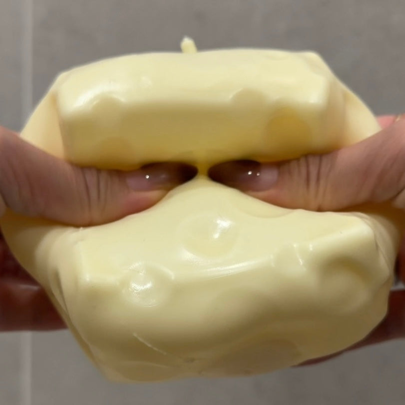 Jumbo cheese squishy stress ball sensory toy being squeezed by hand to show its soft, moldable ASMR texture.