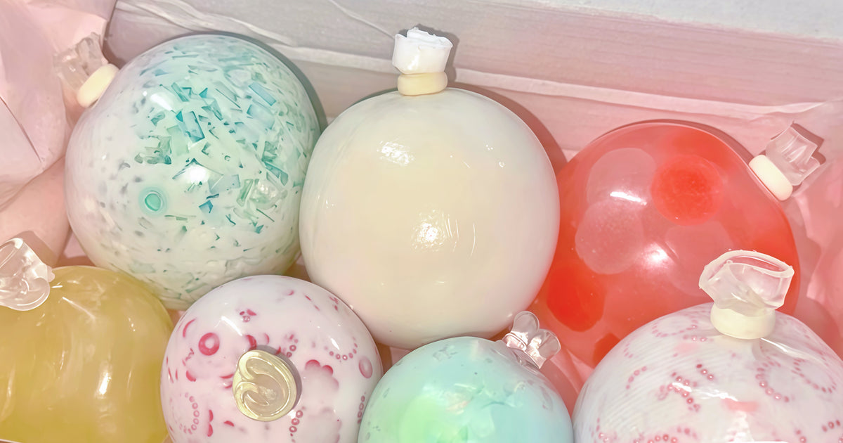 A collection of colorful, translucent handmade squishy stress balls in pastel shades of pink, green, yellow, orange, and white, arranged inside a pink box. They are crunchy ball, butter squishy, cream based and more.