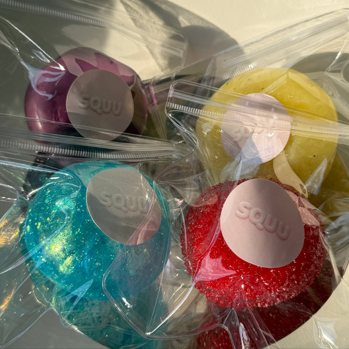 SQUU squishy collection featuring assorted sensory stress balls with soft, slushy, glitter, moldable, and textured fillings in multiple colors.